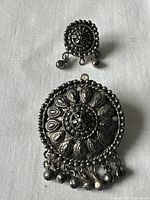 Photo showing front view of both antique brooches-pendants on white fabric background, displaying detailed embossing and dangling charms