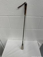 Full view of the 26 inch shoe horn spoon with black and brown handle hanging against a wall.