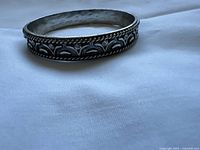 Side view showing the carved flower and vine design with embedded rhinestones on the silver metal bracelet.