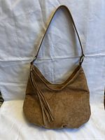 Front view of brown suede small shoulder bag with tassel hanging from strap, plain white backdrop
