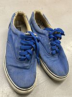 Pair of blue canvas boat shoes with blue laces and white rubber sole, showing minor wear.