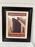 Framed Art Deco TRANSATLANTIQUE poster print featuring ship with Eiffel Tower and Statue of Liberty, front view.