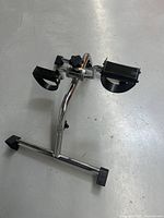 Photo of full under desk bike pedal exerciser showing chrome frame, pedals with straps, adjustment knob, and rubber capped feet.