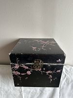 Front view of black wooden box with pink cherry blossom design and metal clasp closure, showing minor edge wear.