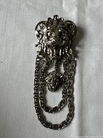 Front view of silver vintage brooch showing lion head and attached chains with small lion head charm