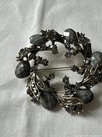 Detailed photo showing back and clasp mechanism of vintage brooch with metal leaves and rhinestones.