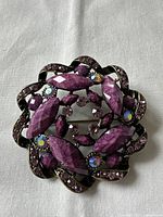 Front view of the vintage brooch showing multicolored rhinestones in purple and iridescent colors set in dark metal with a floral petal pattern.
