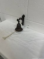 Side view of vintage cast iron bell mounted on wrought iron bracket with white pull cord visible.