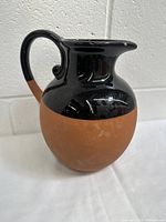 Front angle of vintage clay jug showing two-tone clay and black glaze finish.