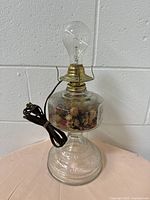 Clear pressed glass vintage electric lamp with brass fitting and bulb placed on a pink cloth against a white wall