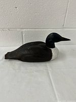 Side view of the wooden loon figurine placed on a white surface against a white wall, showing full body and resting position.