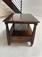 Front view showing the square top, open lower shelf, and single drawer with brass pull handles. Decorative tapered legs and carved details visible.