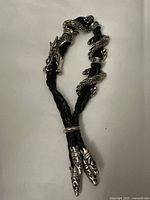 Photo showing the full length of the braided black leather bracelet with a silver-tone dragon design coiling around it and claw-shaped end caps.