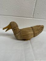 Side angled view of vintage folk art duck figure showing wooden head and straw-wrapped body.