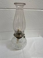 Full view of the vintage glass oil lamp showing clear glass base with diamond pattern, metal burner, and tall glass chimney.