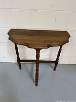 Front view of vintage solid walnut half round wall table showing scalloped edge and turned legs