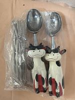 Photo of the vintage ice cream and milkshake set featuring two cow-handle spoons, metal straws, and cleaning brushes packed in plastic.