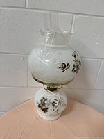 Front and side views of an electric milk glass lamp with brown floral designs and a clear glass chimney, showing the overall shape and decorative details.