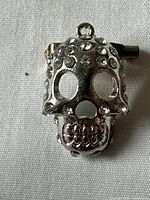 Front view of silver-tone vintage skull pendant with rhinestones, showing hollow eyes and detailed teeth engraving with rhinestones arranged on the forehead area.
