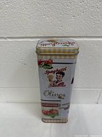 Photo of the front and side of the vintage spaghetti tin showing Italian woman graphic, tomato, olive, and herb illustrations, and "Spaghetti Italiana" text.