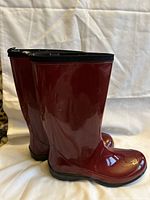 Side view of the pair of glossy red rubber boots showing the sleek design and black sole.