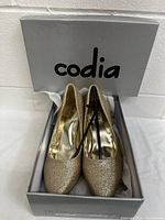 Pair of glittery golden women's heels in open box with Codia branding on box lid and shoe insole.