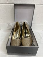 Pair of glitter gold women's heeled shoes inside an open gray box showing the inside and toe front view.