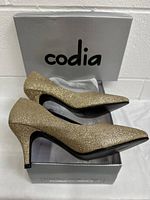 Side view of glitter gold women's heeled shoes on a Codia branded box.