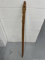 Full view of the 46-inch wooden carved cane leaning against a white wall.