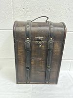 Front view of wooden wine case closed, showing leather straps and metal clasps.
