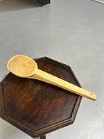 Full view of the wooden spoon showing overall shape, handle with hole, and natural wood color.