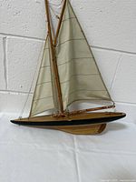 Side view of wooden vintage yacht model sailboat on white background, showing cloth sails, wooden hull with black bottom, and rigging details.