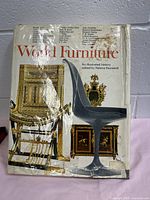 Front cover of the book showing title, subtitle, editor name, damaged and stained dust jacket with images of various furniture pieces.