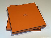Two stacked Hermès orange scarf boxes photographed on white background showing the logo and orange color.