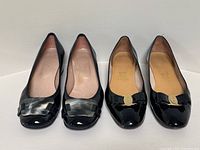 Two pairs of women's black patent leather pumps placed side by side showing the toe view and decorative bows.