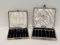 Two hinged boxes open showing both sets of sterling silver cocktail picks