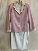 Full view of the pink and cream jacket hanging over the cream skirt on hanger, showing the full outfit.