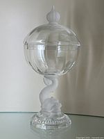 Full view of the crystal pedestal dish showing the dolphin figure base, clear ribbed bowl and onion-shaped finial lid.