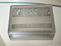 Full view of the antique rectangular smoky satin crystal box showing the cavalry battle scene relief on the lid and Greek key decorative border band, placed on a reflective surface.