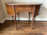 Front view of kidney-shaped desk showing overall shape, painted drawer center, carved legs
