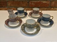 Four antique Limoges demitasse cups and saucers arranged with four different lace pattern colors including some spoons in one cup.