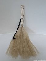 Full photo showing the entire fly whisk with carved bone handle and light horse hair bristles hanging down spread out broadly.