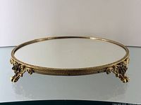 Low-angle view of round gilt frame tray with mirrored surface and decorative feet