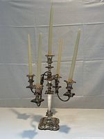 Full view of silver plated candelabra holding five taper candles, showing intricate design and curved arms.