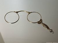 Full view of folding lorgnette with round lenses and attached handle resting on reflective surface
