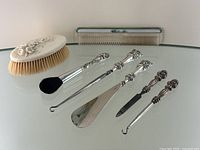 Overview of carved brush, comb, and silver-handled vanity tools including powder brush, two hooks, shoehorn, and nail cleaner