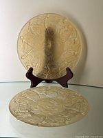 Two clear gold satin glass plates, one upright on a stand and one flat