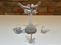 Front view of three glass bird sculptures perched on base and one smaller bird figurine placed on surface.