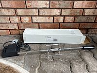 Electric BBQ rotisserie laid out in front of a brick wall, showing the rotisserie spit, motor, and original box.
