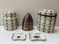 Front view of full set including two bee patterned porcelain jars with lids, silver plated beehive-shaped candle holder, and two small rectangular porcelain dishes with insect motifs
